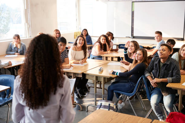 Rear View Of Female High School Teacher Standing At Front Of Class Teaching Lesson Rear View Of Female High School Teacher Standing At Front Of Class Teaching Lesson high school stock pictures, royalty-free photos & images
