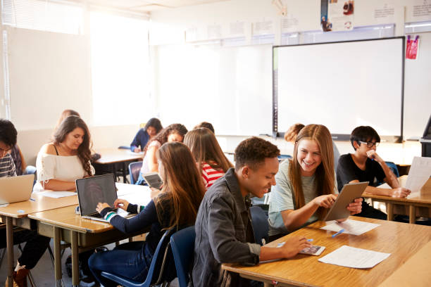 vista de gran angular de los estudiantes de secundaria que están sentados en los escritorios en classroom usando laptops - salón de clase fotografías e imágenes de stock