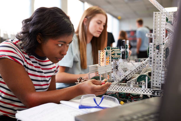 two female college students building machine in science robotics or engineering class - stem imagens e fotografias de stock