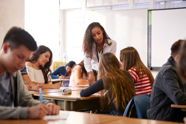 istock Female High School Teacher Standing By Student Table Teaching Lesson 1133836622