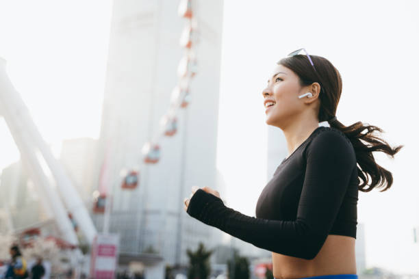 energetic young sports woman listening music through in-ear headphones while jogging in urban city - self improvement audio imagens e fotografias de stock