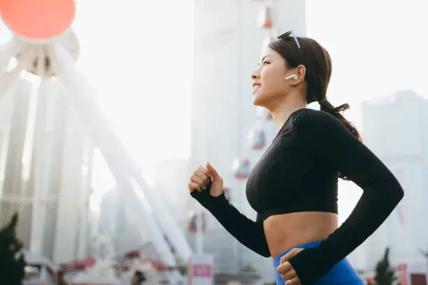 Energetic young sports woman listening music through in-ear headphones while jogging in urban city