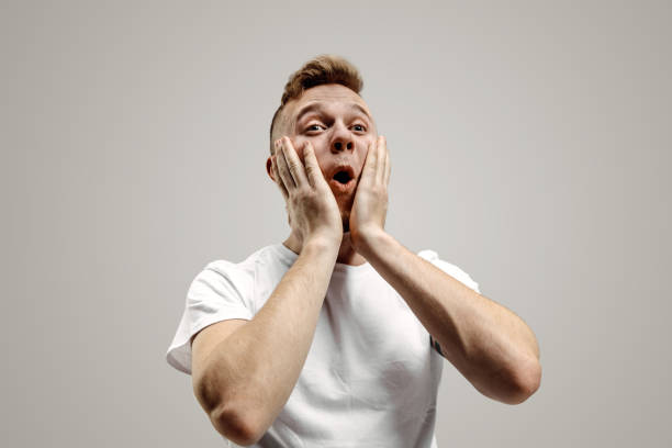 istock The young attractive man looking suprised isolated on gray 1133842449