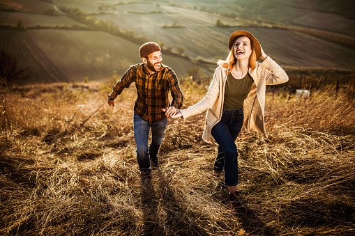 Carefree couple having fun while holding hands and running in autumn day on the hill.