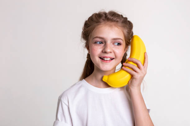 istock Joyful long-haired child with blue eyes carrying plastic banana 1133845452