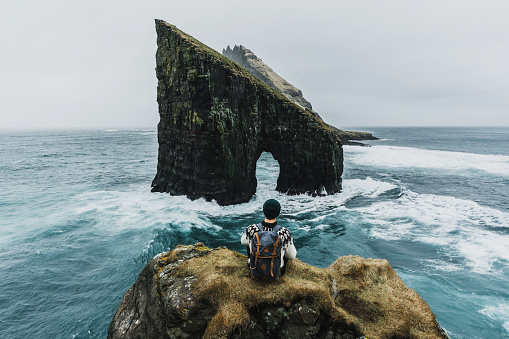 Hombre en suéter de punto mirando a la vista del arco Drangarnir en las Islas Feroe photo