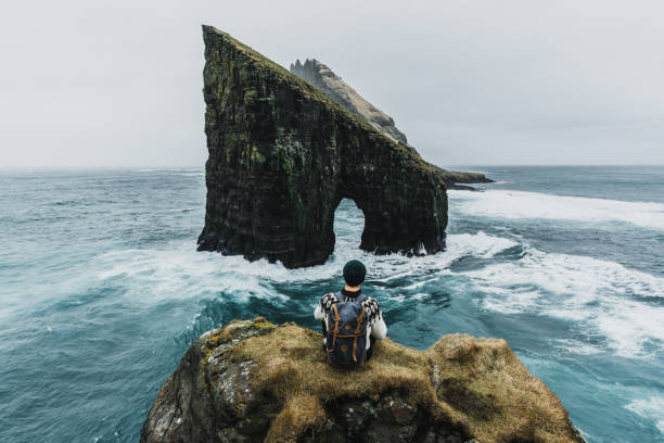 Man in knitted sweater looking at view of Drangarnir arch in Faroe Islands Young Caucasian man  in knitted sweater looking at view of Drangarnir arch in Faroe Islands faroe islands photos stock pictures, royalty-free photos & images