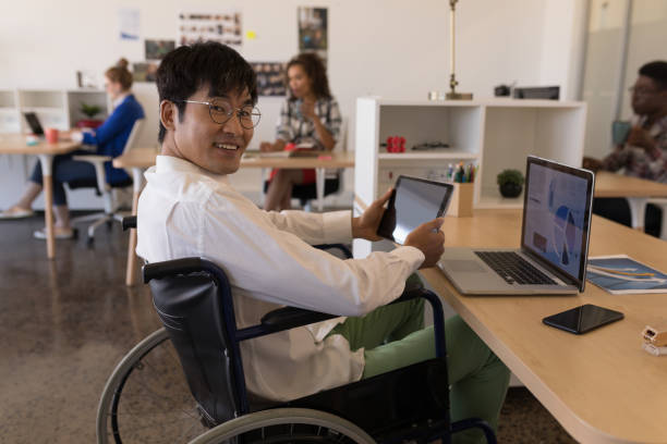 Disabled male executive using digital tablet at desk Side view of young disabled Asian male executive using digital tablet at desk in modern office physical disability photos stock pictures, royalty-free photos & images