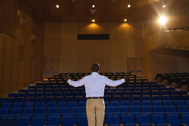 istock Businessman with arm stretched out standing in a auditorium 1133853327