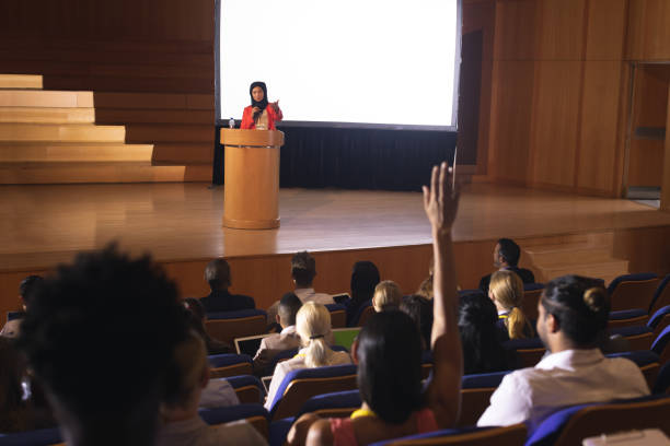 istock Woman sitting in audience raising hand for asking question 1133855326