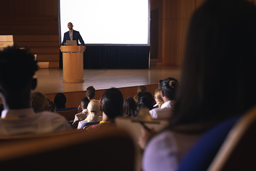 Front view of mixed race businessman giving speech in front of audience in the auditorium