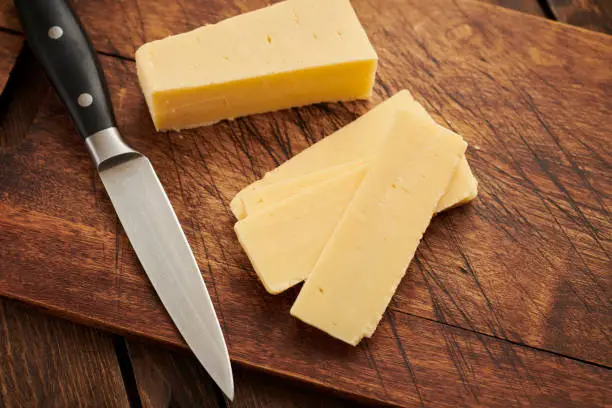 Sliced cheddar cheese on an aged wood chopping board.