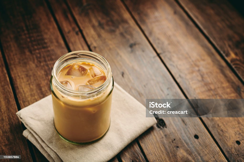 Mason Jar filled with iced coffee with double cream on a rustic table top. Coffee - Drink Stock Photo