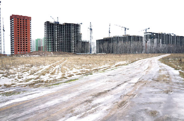 Construction new buildings in wasteland, frozen country road, crane, winter, ground, snow, white cloudy sky background