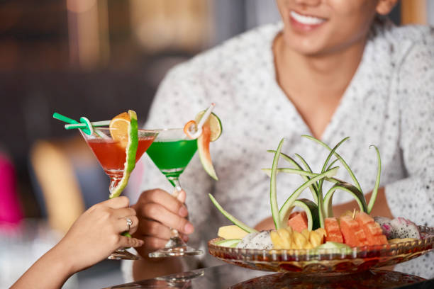 Close-up of young couple holding colorful cocktails decorated with fruits and toasting at restaurant
