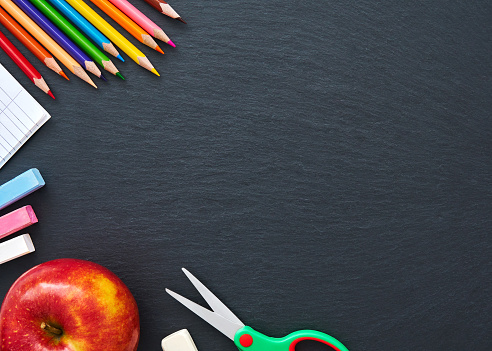 The texture of the school supplies on the graphite board closeup. Red apple, colored pencils, crayons, scissors, glue. Bright abstract background ideal for any design