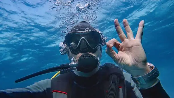 Man scuba diver underwater showing signal OK. Descending.