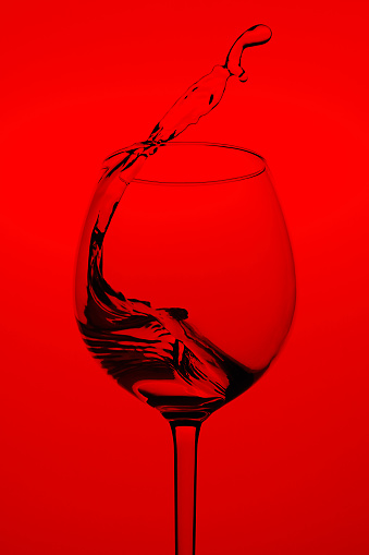 Wine glass with water in motion, splash on a red background