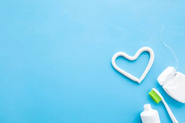 Photo of Toothbrush, white tube of toothpaste, container of dental floss on pastel blue background. Heart shape created from paste. Love healthy teeth concept. Empty place for text, quote, sayings or logo.