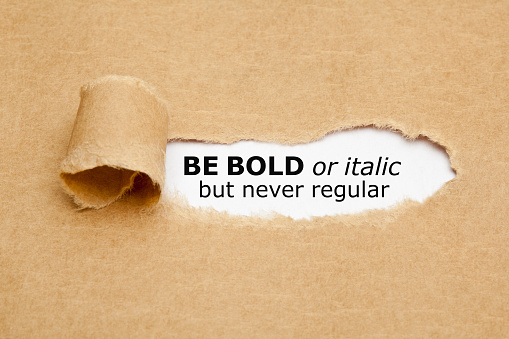 Inspirational quote Be Bold Or Italic But Never Regular appearing behind torn paper. Concept about the importance of being different and standing out from the crowd.