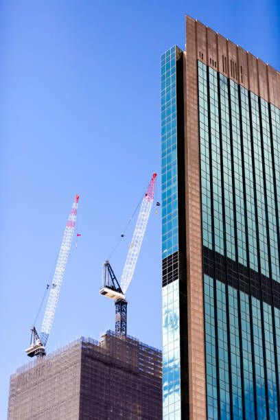 Construction of skyscraper with tower cranes, blue sky background with copy space, full frame vertical composition