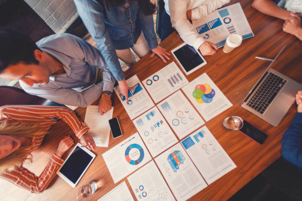 istock Paperwork and hands on a board room table at a business presentation or seminar. The documents have financial or marketing figures, graphs and charts on them. There is a digital tablet and laptop on the table. Multi ethnic group including Asian, Caucasian 1133887507