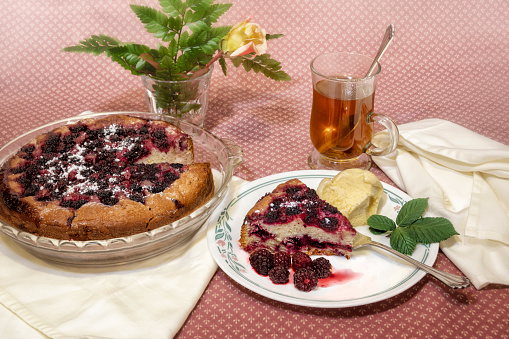 Home made wild berries cake and slice with tea and rose flower on pink tablecloth