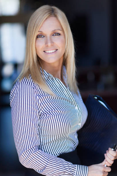 Blond mature businesswoman smiling at the camera. Office background. She is holding a document stock photo