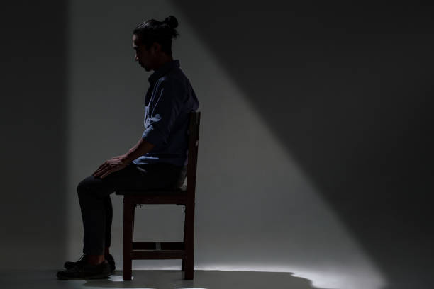 Spain. Mature man with a beard and short hair, wearing a brown polo shirt, sitting against a wall, absorbed in contemplative thought.