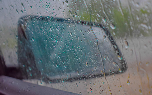 Raindrops flowing down passenger window of car during a summer storm.