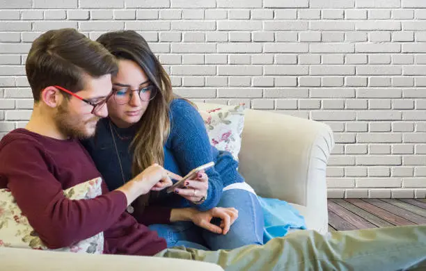 lovely young couple using smart phone in living room at home