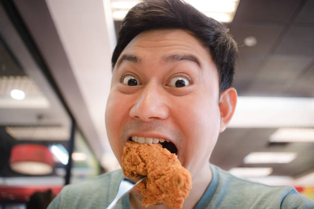 istock Funny face Asian man eat fried chicken. 1133918506