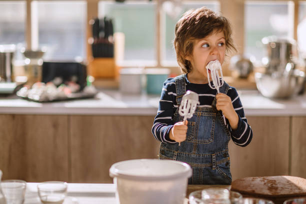 Cute Kid Tasting Whipped Cream of Egg Beater Cute Kid Tasting Whipped Cream of Egg Beater In Kitchen, Making Adorable Funny Faces in Manner of Sweet Taste licking stock pictures, royalty-free photos & images