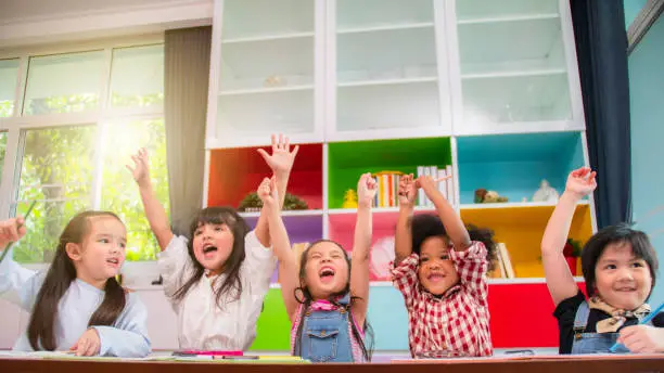 Photo of Group of multi-ethnic five little kids children African American, asian and Caucasian happiness together with friend to draw colour pencil to full colour of picture in living room or class room