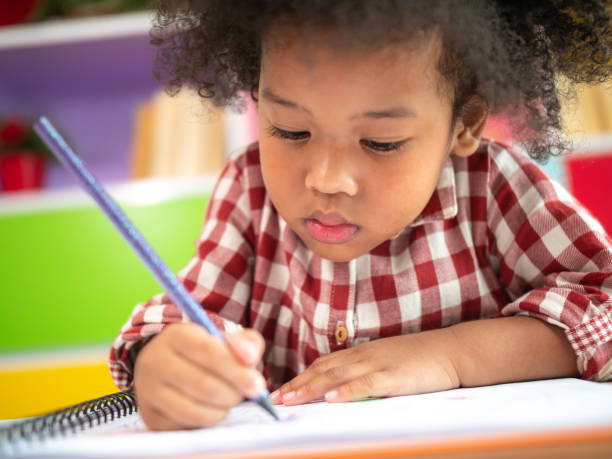 Close up of shot Cute little African American kid concentrate draw full colour of picture with colour pencil with friend in backgrounds. Kindergarten school concept, children education, preschool.