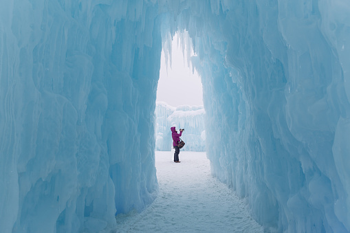 horizontal image of a caucasian woman standing in an ice castle in the entrance way and taking pictures on a cold winter day.