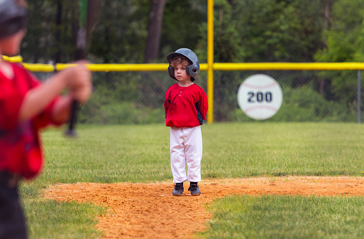 A little boy stands on third base waiting for the batter (foreground) to hit the ball.