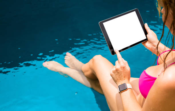 istock Woman by the pool holding tablet horizontally with empty mock up screen. 1133938286
