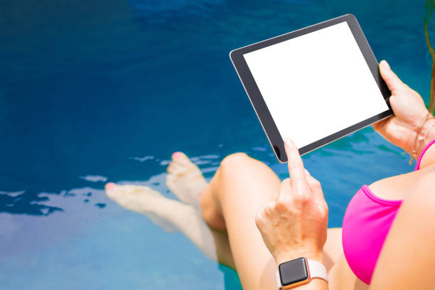 istock Female by the pool holding tablet with empty white screen. 1133938488