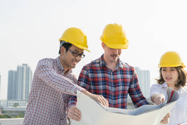 istock Multiethnic group of young civil engineers , worker and architects discussing on drawing/blueprint construction with highrise building background, wearing safety yellow helmet. Inspection concept. 1133938504