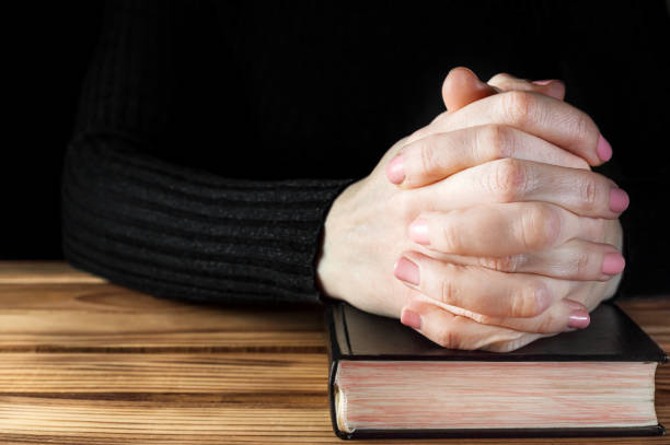 istock Woman praying over table with Holy Bible. Close up. Space for text. 1133944478