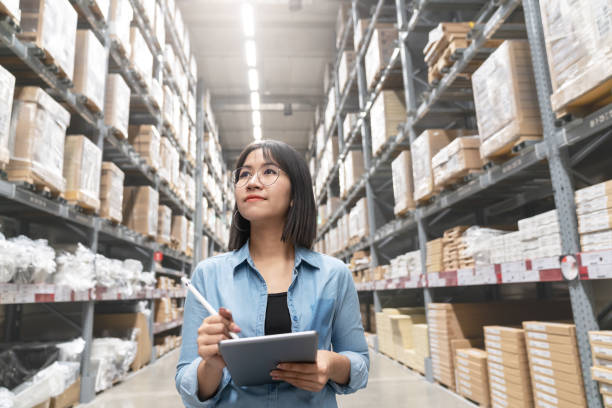 candid do auditor asiático atrativo novo da mulher ou do trabalho da equipe de funcionários do estagiário que olham acima balanço o inventário na loja do armazém pela tabuleta do computador com opinião de ângulo larga. proprietário asiático ou co - armazém comercial - fotografias e filmes do acervo