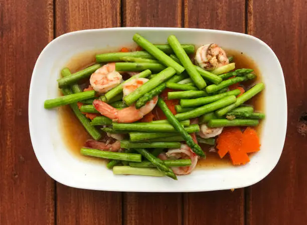 Stir-Fired Asparagus with Shrimp in white dish on wooden table, delicious of  Thai food , Name of this menu in Thailand : "Nor mai Fa-rang pad kung".