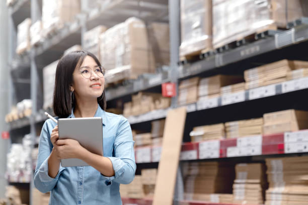 istock Young attractive asian worker, owner, entrepreneur woman holding smart tablet computer looking side up above shelf with efulfillment service business warehouse online concept. Asian sme merchandise. 1133950549
