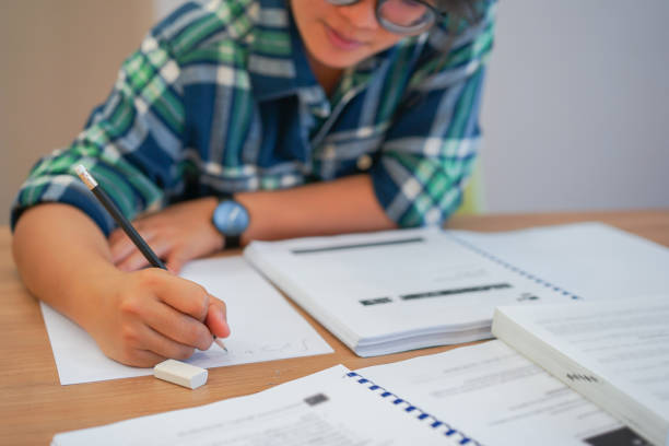 close up young asian student girl using pencil for writing formula of calculus on paper for do homework in library silent zone with textbook , campus lifestyle concept - livro de textos imagens e fotografias de stock