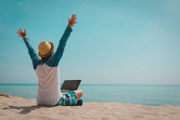 istock happy young man working on laptop at beach 1133955672