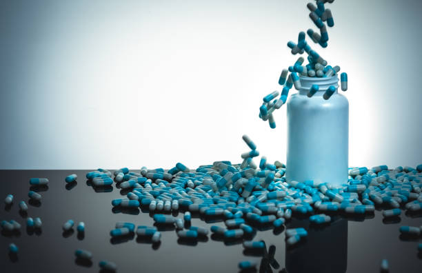 Pouring blue-white capsule pill to white bottle and black table. Antibiotic drug overuse. Antibiotic drug use with reasonable. Antibiotic drug resistance. Pharmaceutical industry. Antimicrobial pill. verter la píldora de la cápsula azul-blanca a la botella blanca y a la tabla negra. uso excesivo de fármacos antibióticos. uso antibiótico de la droga con razonable. farmacorresistencia antibiótica. industria farmacéutica. píldora antimicrobiana.