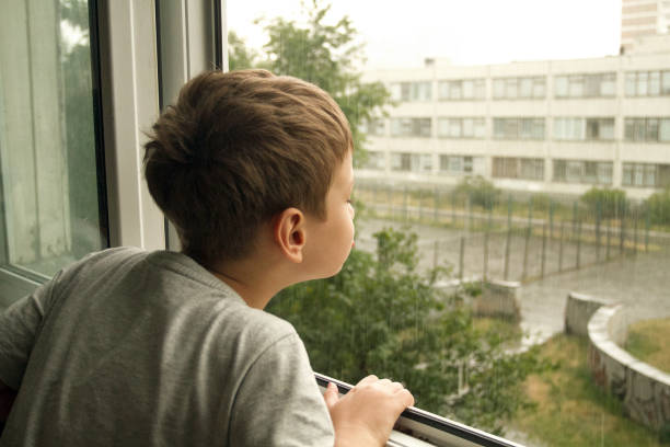 istock Boy looking through the window. Boy watching the rain through the window 1133960039