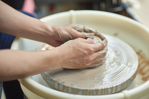 Cropped hands of young man making clay product. Male is using pottery wheel. He is learning in workshop.