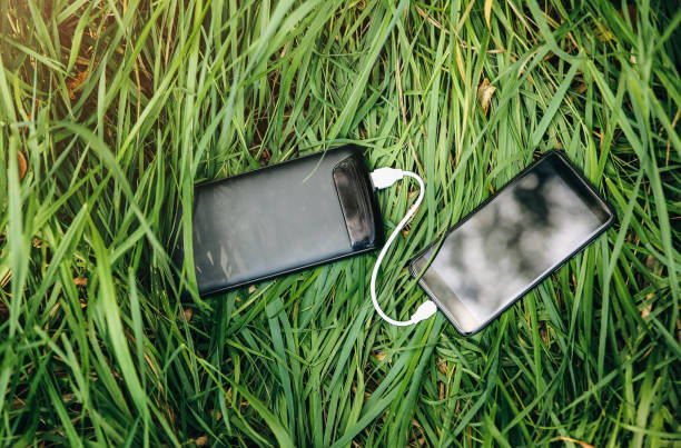 istock Smartphone and black power bank are lying with USB on green grass. Modern information technology photo. Battery charger in the summer nature. Travel with your phone. 1133966975